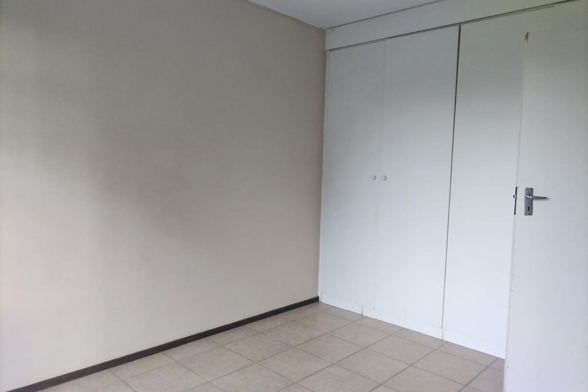 An empty bedroom featuring neutral tiled flooring and built-in cupboards, providing a blank canvas for personalization.