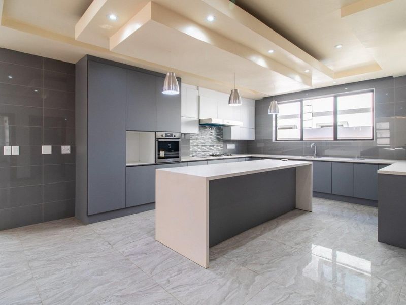Modern kitchen featuring sleek grey cabinetry, a central island with stone countertops, built-in appliances, and high-quality tiled flooring with recessed ceiling lighting.