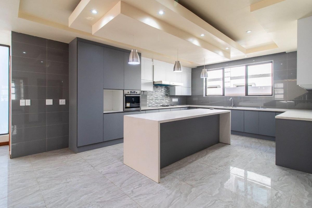 Modern kitchen featuring sleek grey cabinetry, a central island with stone countertops, built-in appliances, and high-quality tiled flooring with recessed ceiling lighting.