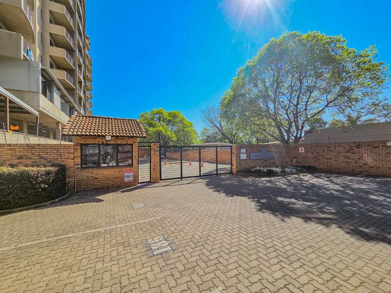 The entrance to the apartment complex features a secure gated access point, a guard house, and paved driveway area with perimeter electric fencing.