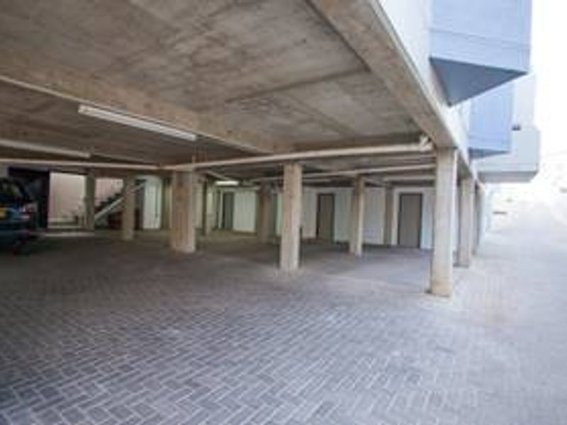A covered parking area featuring concrete structural pillars and ceiling with paved flooring, providing sheltered vehicle storage.