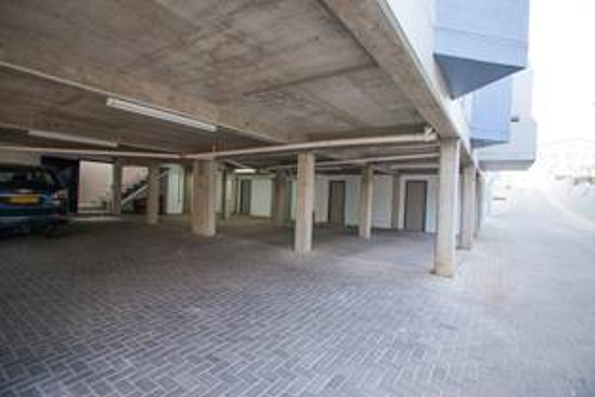 A covered parking area featuring concrete structural pillars and ceiling with paved flooring, providing sheltered vehicle storage.