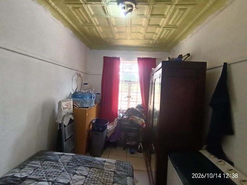 A small bedroom featuring a decorative pressed metal ceiling and security bars on the window, currently requiring cosmetic updates and repairs to walls.
