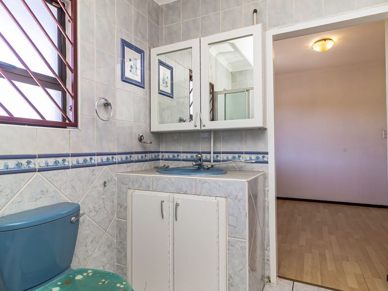 A functional bathroom featuring tiled walls, a built-in vanity with basin, and a toilet, with security bars on the window.