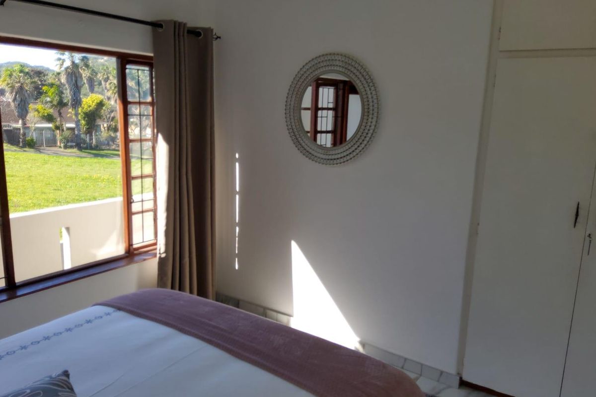 A bright bedroom featuring built-in cupboards, tiled flooring, and a large window offering views of the garden.