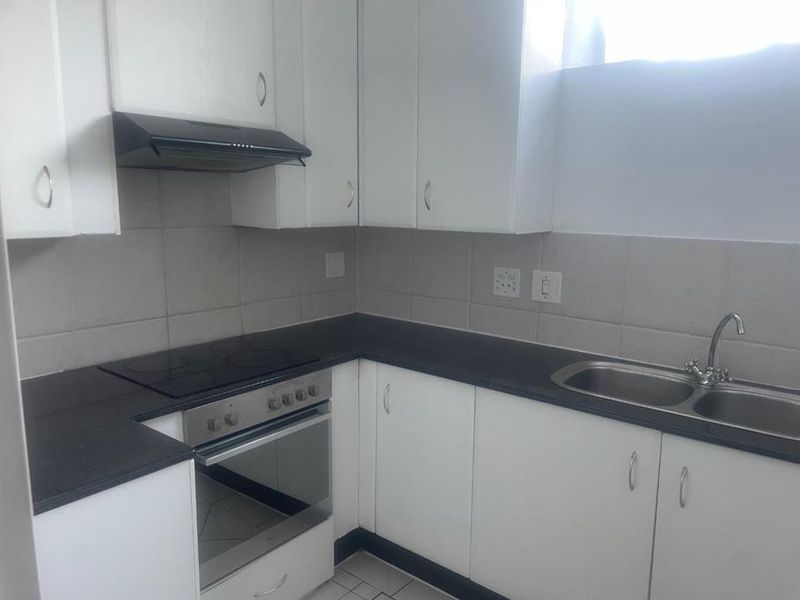 A functional kitchen featuring white cabinetry, dark countertops, a built-in oven with electric hob, extractor fan, and a double sink with tiled backsplash.