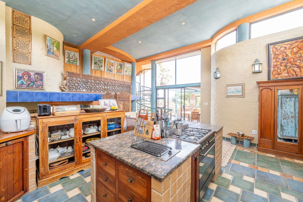Spacious kitchen featuring a central island with gas hob, tiled flooring, and large windows providing natural light and access to the outdoor area.