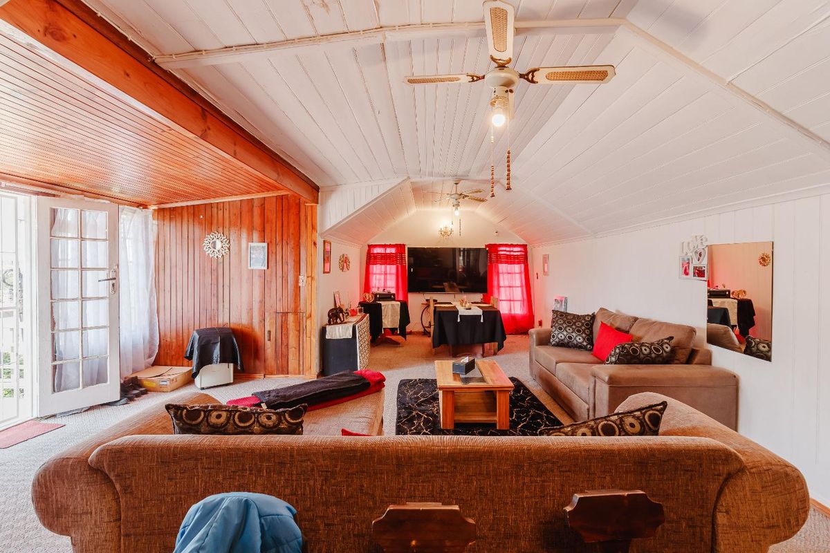 Spacious living room featuring a vaulted ceiling with integrated fans, timber wall paneling, and access to an exterior area through a classic french door.