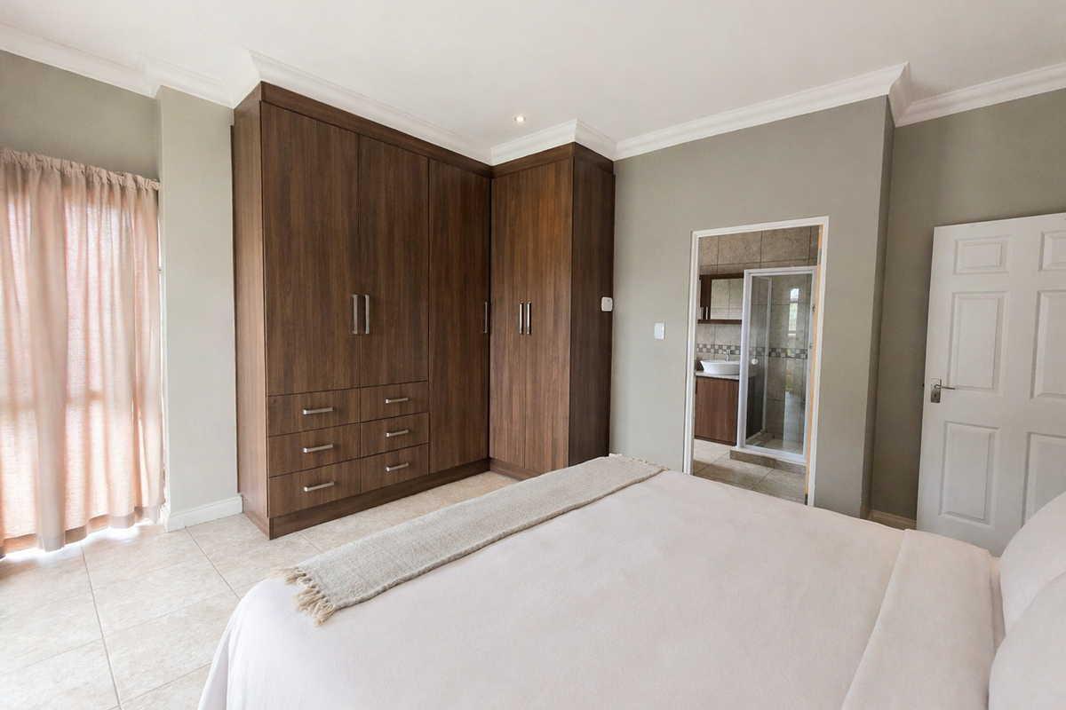 Spacious bedroom featuring built-in wooden cabinetry, tiled flooring, and an en-suite bathroom with a shower.