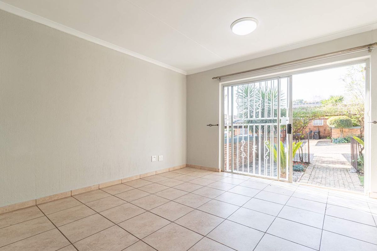 A bright, empty living room featuring neutral tiled flooring and a sliding glass door with security gate leading to the rear garden.