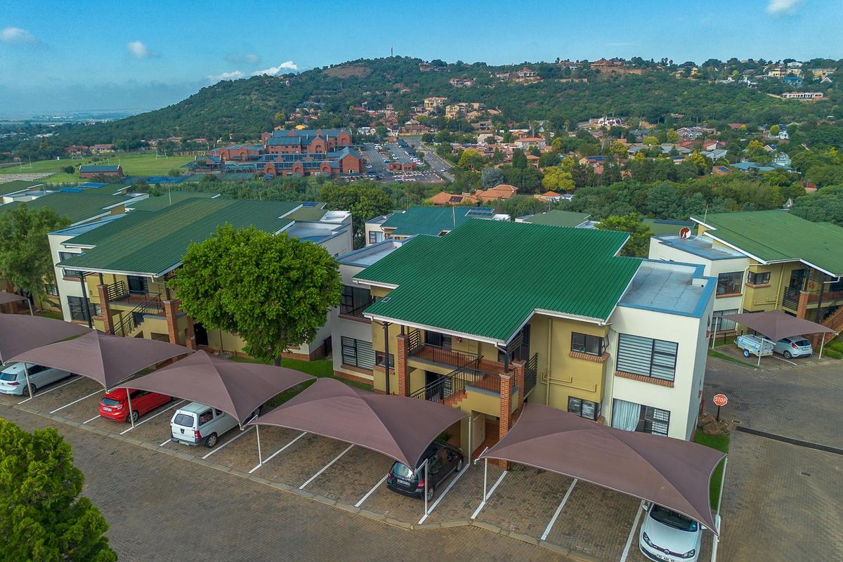Aerial view of the apartment complex featuring green metal roofing, paved parking areas with shade cloth carports, and surrounding residential landscape.