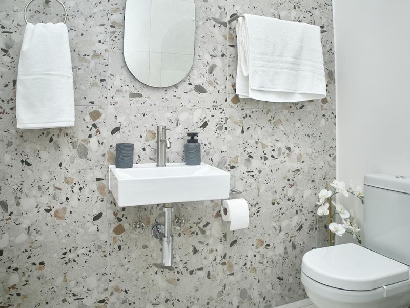 Modern bathroom featuring stylish terrazzo wall tiling, a wall-mounted basin with chrome fixtures, and a contemporary dual-flush toilet.