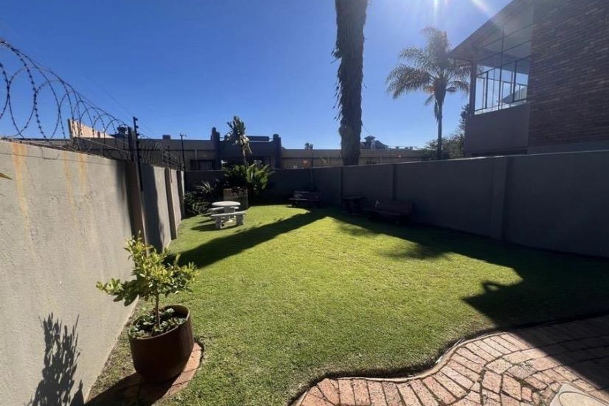 A private rear garden featuring a well-maintained lawn, paved walkway, and high perimeter walls secured with electric fencing.