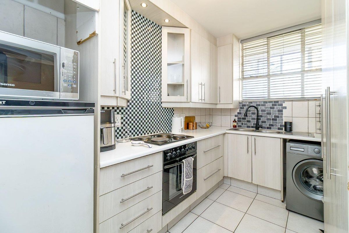 Compact kitchen featuring light wood-grain cabinetry, a built-in oven and hob, tiled backsplash, and integrated laundry plumbing.