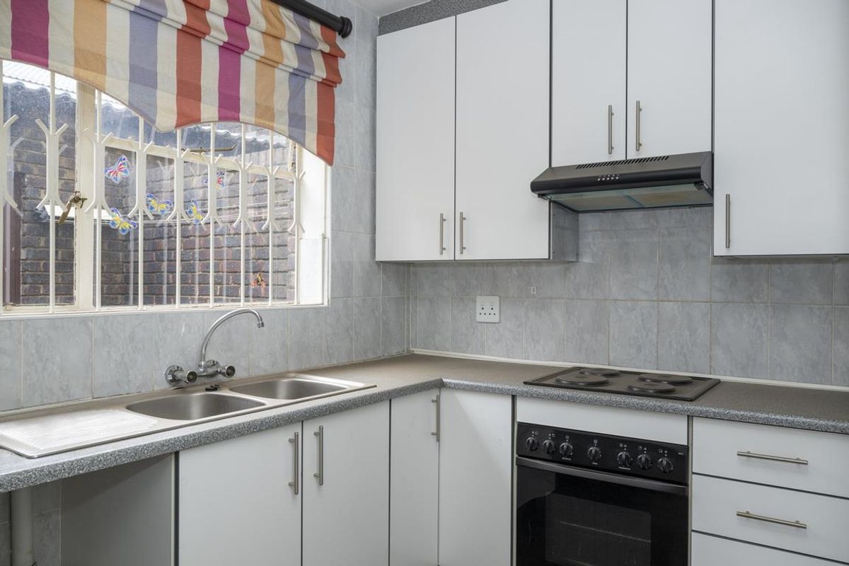 A functional kitchen featuring white cabinetry, a double stainless steel sink, a built-in oven with electric hob, and an extractor fan.