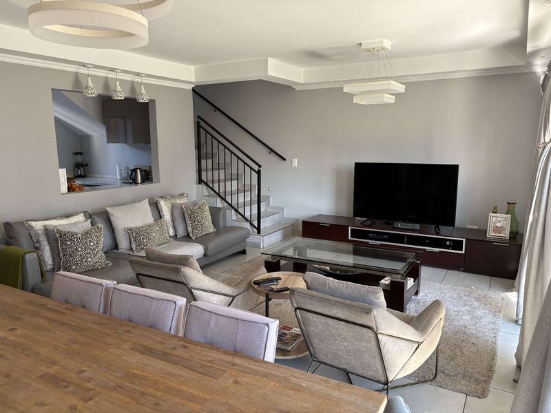 An open-plan living area featuring tiled flooring, a staircase with a metal balustrade, and a convenient pass-through window connecting to the kitchen.