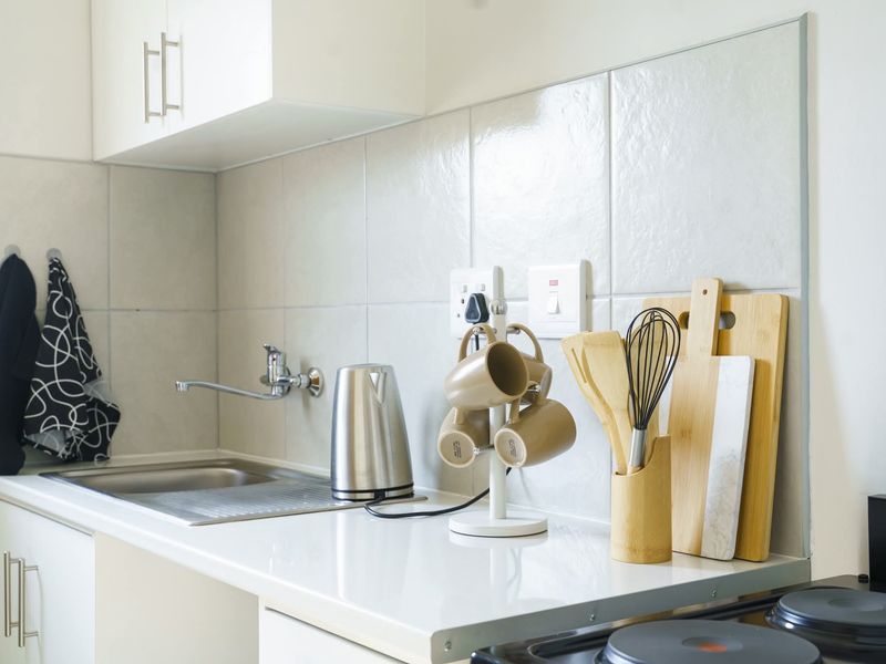 A clean and functional kitchen area featuring a stainless steel sink, tiled backsplash, and built-in cabinetry with a modern laminate countertop.