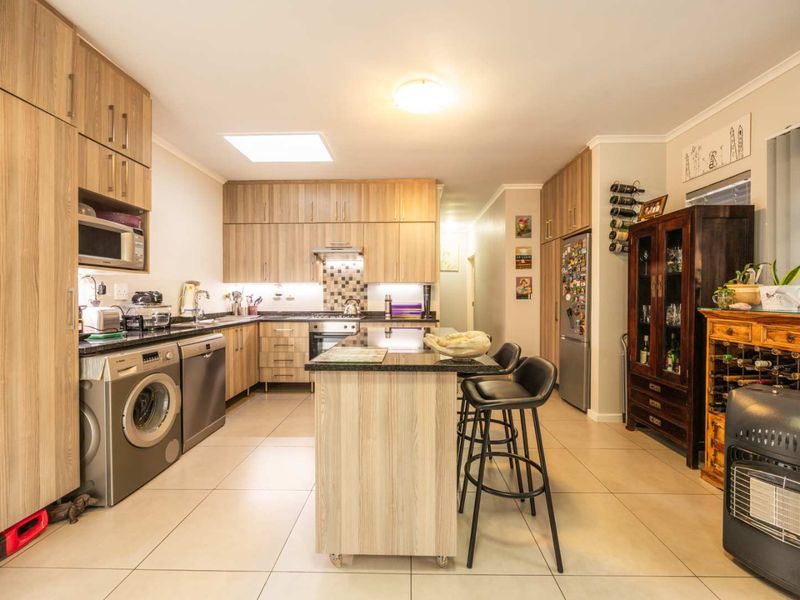 Modern kitchen featuring light wood cabinetry, granite countertops, integrated appliances, and a central island, complemented by a skylight and tiled flooring.