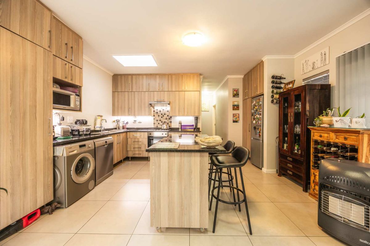 Modern kitchen featuring light wood cabinetry, granite countertops, integrated appliances, and a central island, complemented by a skylight and tiled flooring.
