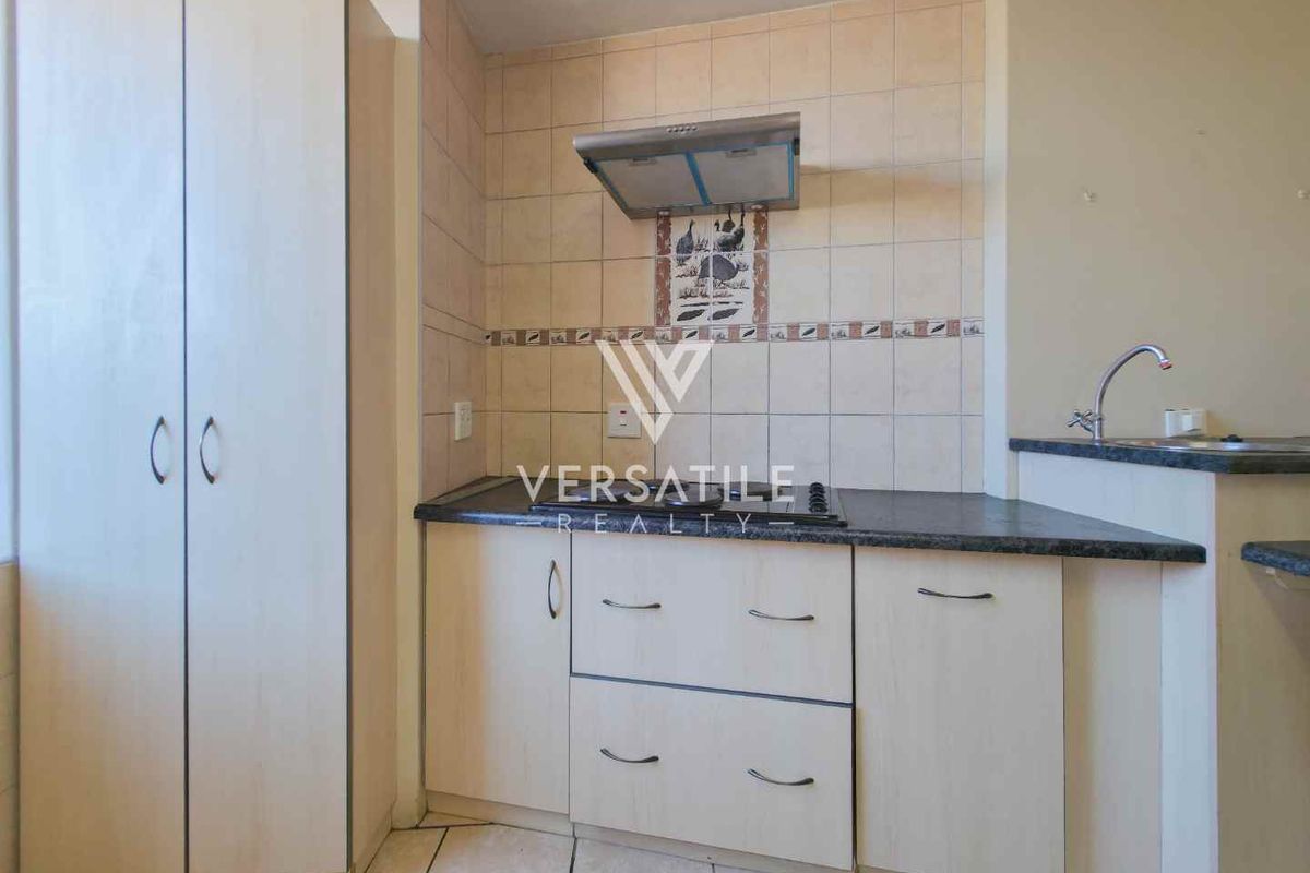 Compact kitchen featuring laminate cabinetry, tiled backsplash, stainless steel extractor fan, and a built-in cupboard for additional storage.