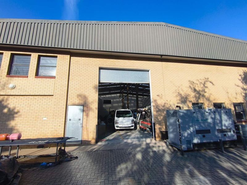 Front elevation of an industrial warehouse featuring a large roller shutter door, brick facade, and paved exterior access area.
