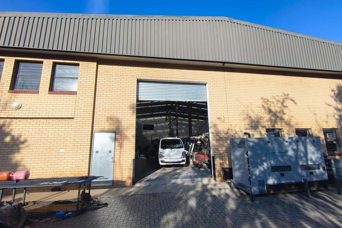 Front elevation of an industrial warehouse featuring a large roller shutter door, brick facade, and paved exterior access area.