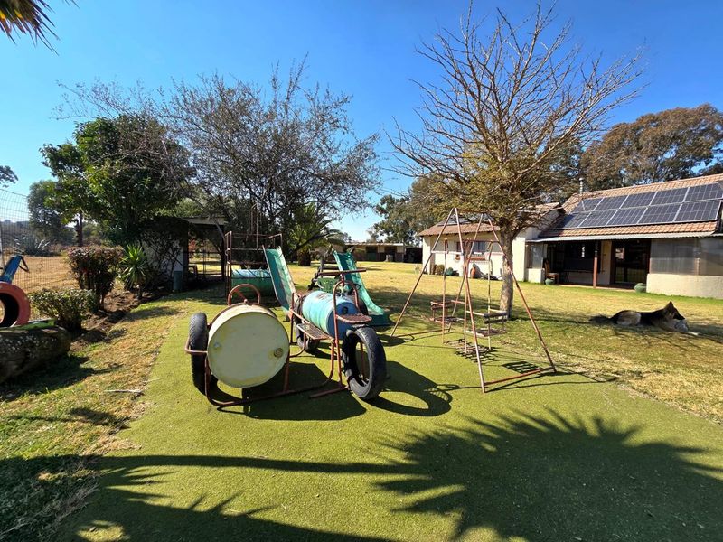 Spacious garden area featuring artificial lawn, mature trees, and a residential building equipped with roof-mounted solar panels.
