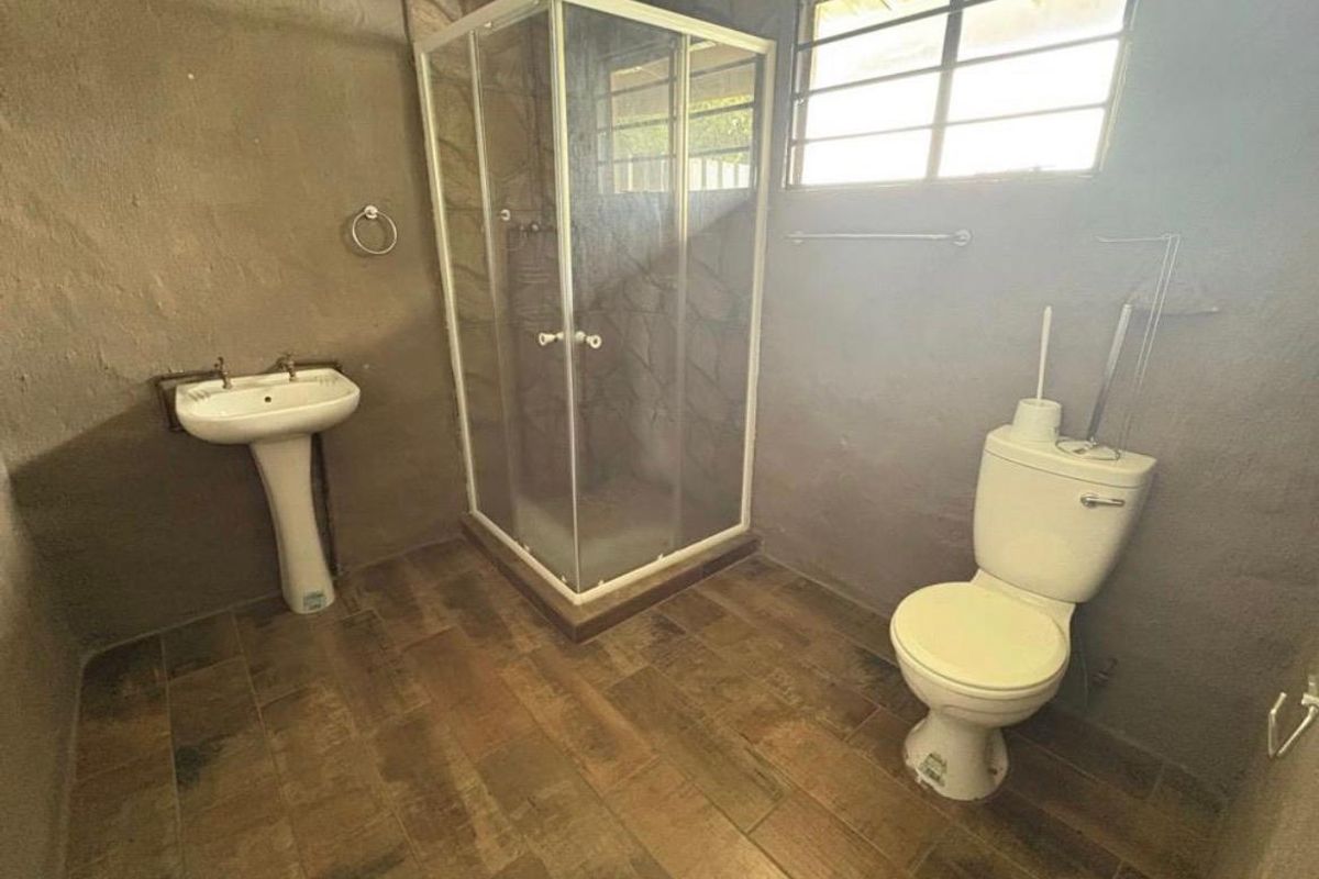 A functional bathroom featuring a corner shower enclosure, pedestal basin, and toilet with wood-look tiled flooring and textured wall finishes.