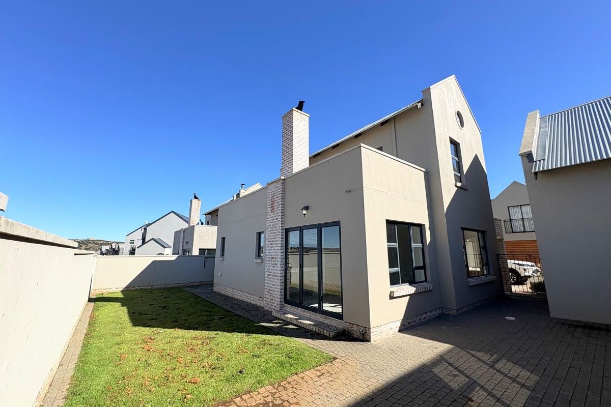 Rear view of the townhouse featuring a paved courtyard, small lawn area, and a prominent brick chimney stack.