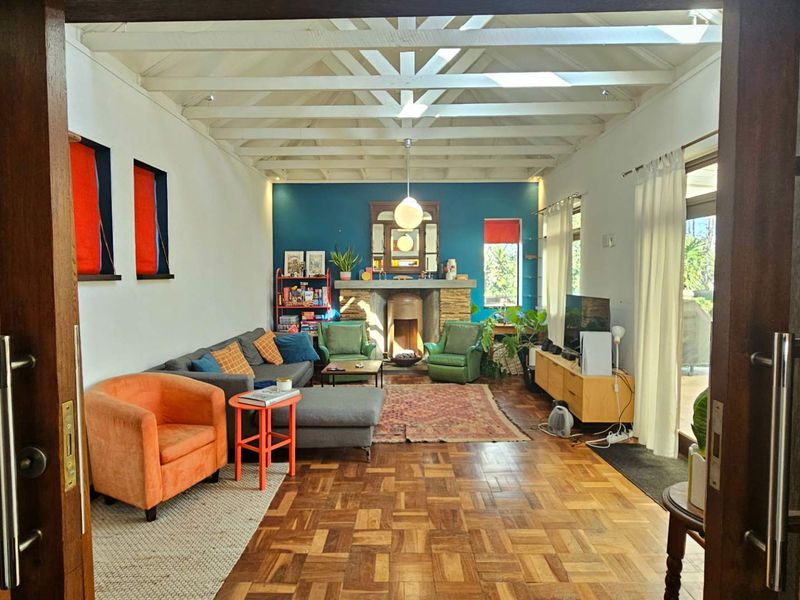 Spacious living room featuring classic parquet flooring, exposed timber ceiling beams, a stone fireplace, and natural light from skylights and sliding glass doors.