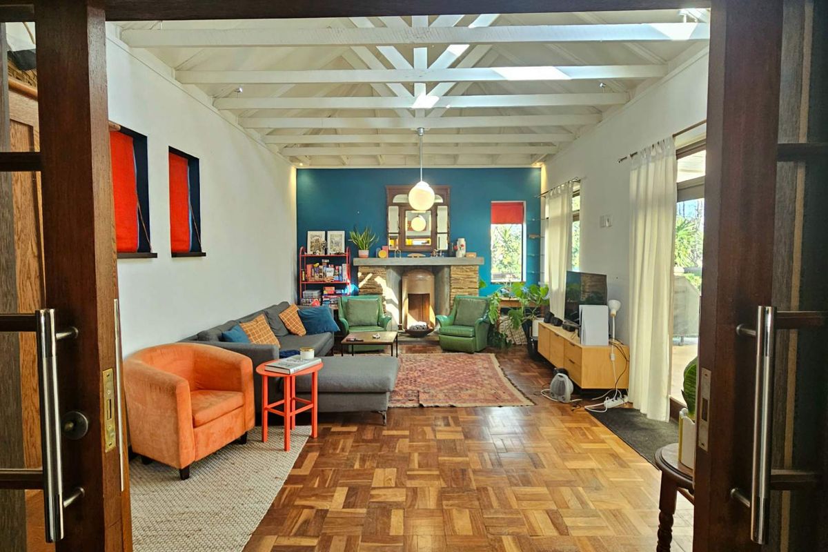 Spacious living room featuring classic parquet flooring, exposed timber ceiling beams, a stone fireplace, and natural light from skylights and sliding glass doors.