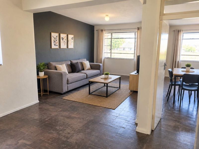 Open plan living and dining area featuring classic parquet flooring and large steel frame windows, providing a bright and functional layout.