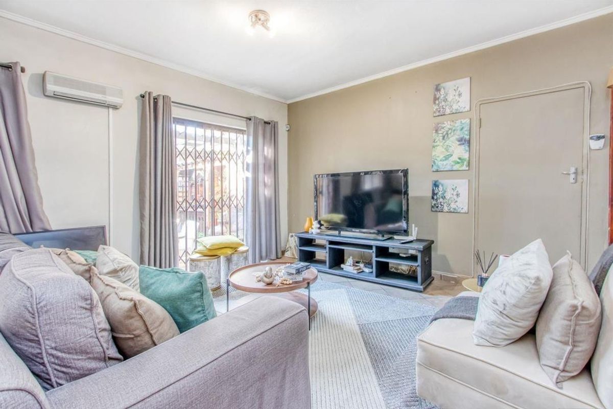 A comfortable living room featuring tiled flooring, a wall-mounted air conditioning unit, and a sliding glass door with security gate leading outdoors.