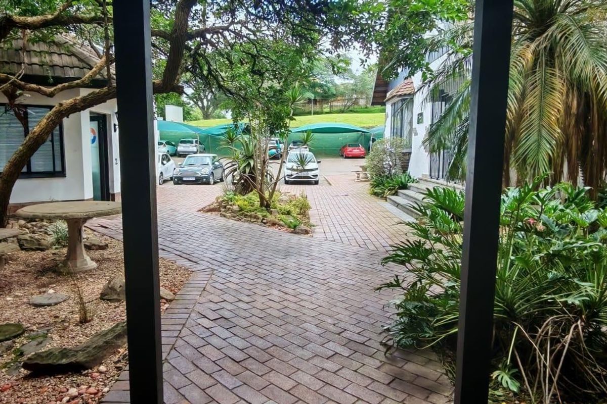A well-maintained courtyard area featuring brick paving, mature trees, and established garden beds, providing a pleasant outdoor space for the retail property.