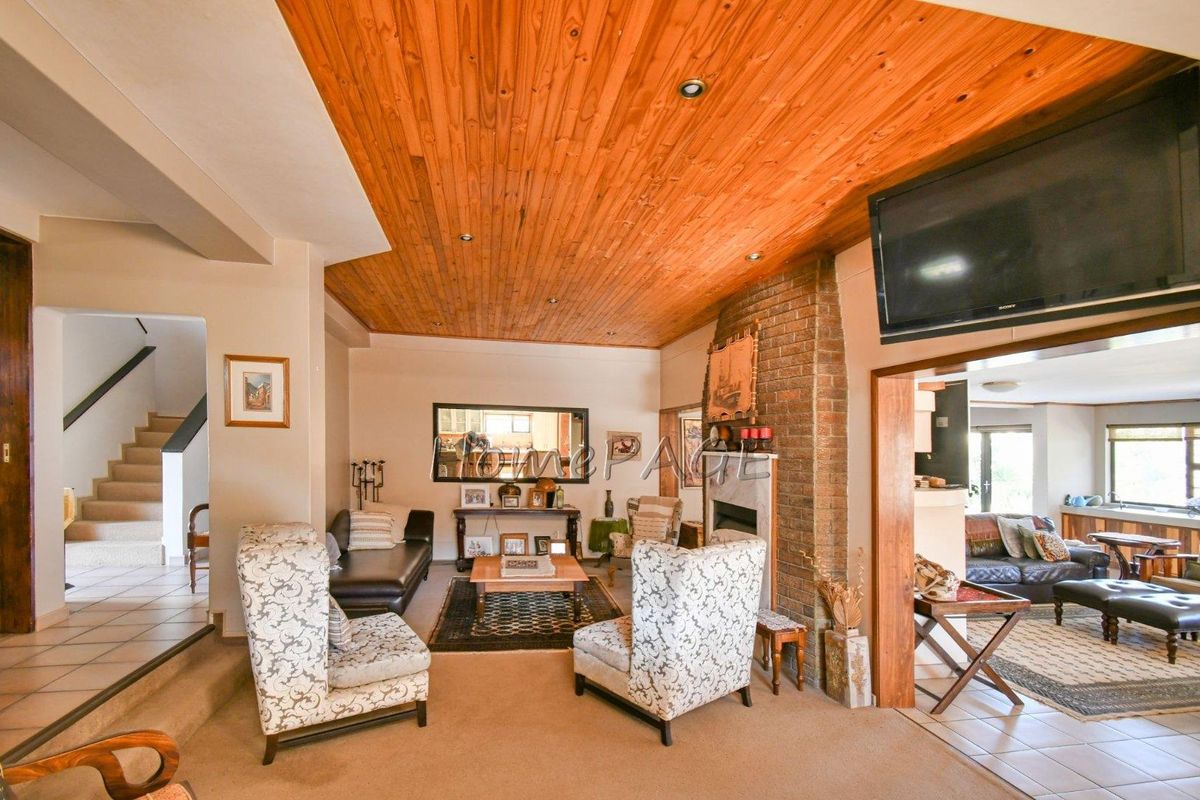 Spacious living area featuring a prominent brick fireplace, warm timber-clad ceiling with recessed lighting, and an open-plan layout connecting to adjacent living spaces.