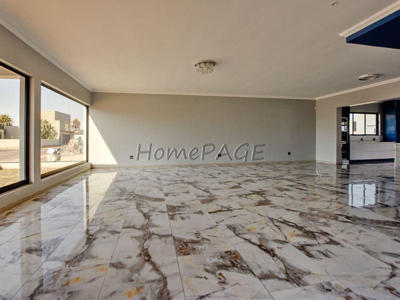 Spacious open-plan living area featuring high-quality marble-look tiled flooring, large windows providing ample natural light, and a seamless transition to the kitchen area.