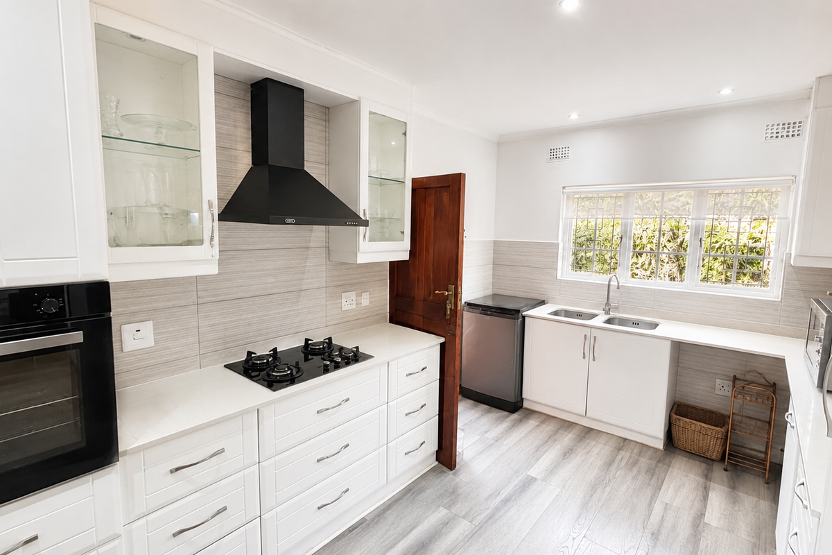 Modern kitchen featuring white cabinetry, stone countertops, built-in oven, gas hob, extractor fan, and a double sink with a window view.