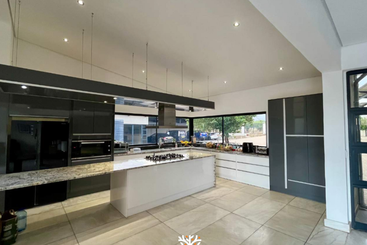 Modern open-plan kitchen featuring a large central island, stone countertops, integrated cabinetry, built-in oven, and a gas hob with an overhead extractor fan.