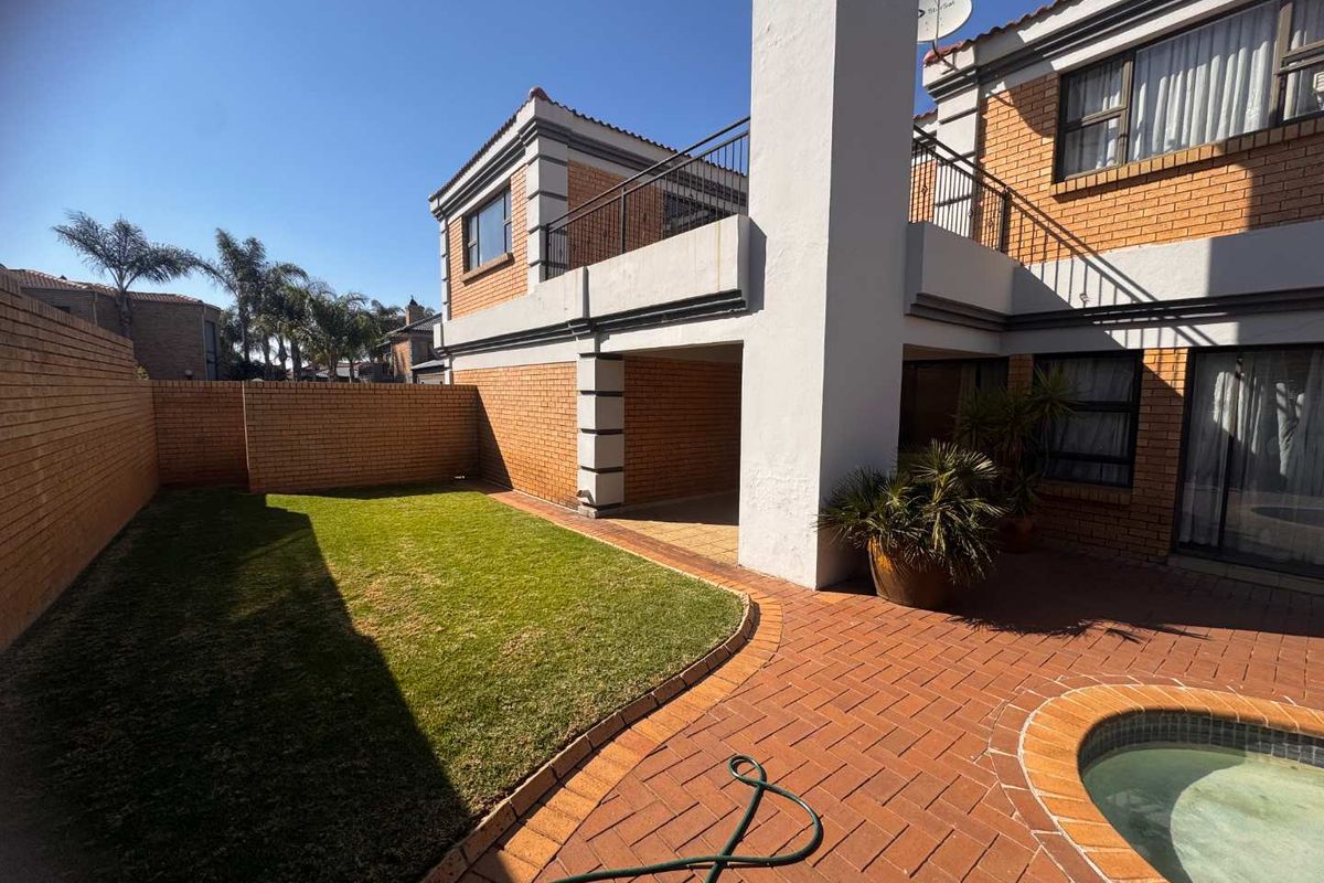 Rear exterior view featuring a brick facade, paved patio area, swimming pool, and a small private lawn with a balcony above.