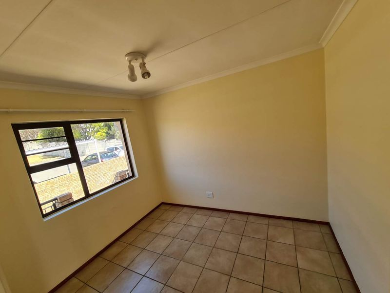 A clean, empty bedroom featuring neutral walls, tiled flooring, and an aluminium-framed window providing natural light.