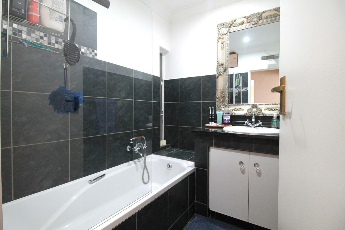 A modern bathroom featuring dark wall tiling, a built-in bathtub with a glass screen, and a vanity cabinet with a granite countertop.