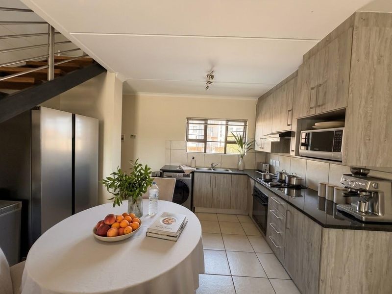 Modern kitchen featuring wood-grain cabinetry, granite countertops, integrated appliances, and tiled flooring, conveniently located adjacent to an open-plan dining area and staircase.