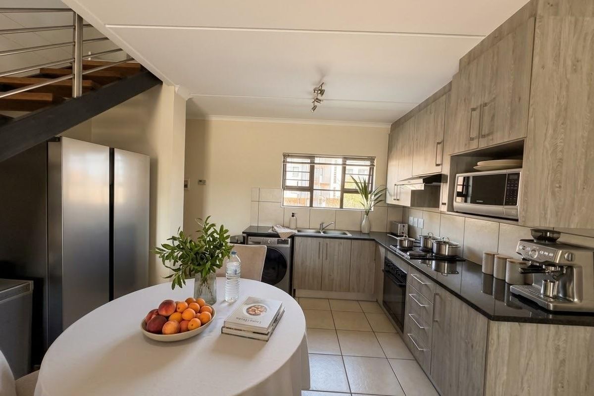 Modern kitchen featuring wood-grain cabinetry, granite countertops, integrated appliances, and tiled flooring, conveniently located adjacent to an open-plan dining area and staircase.