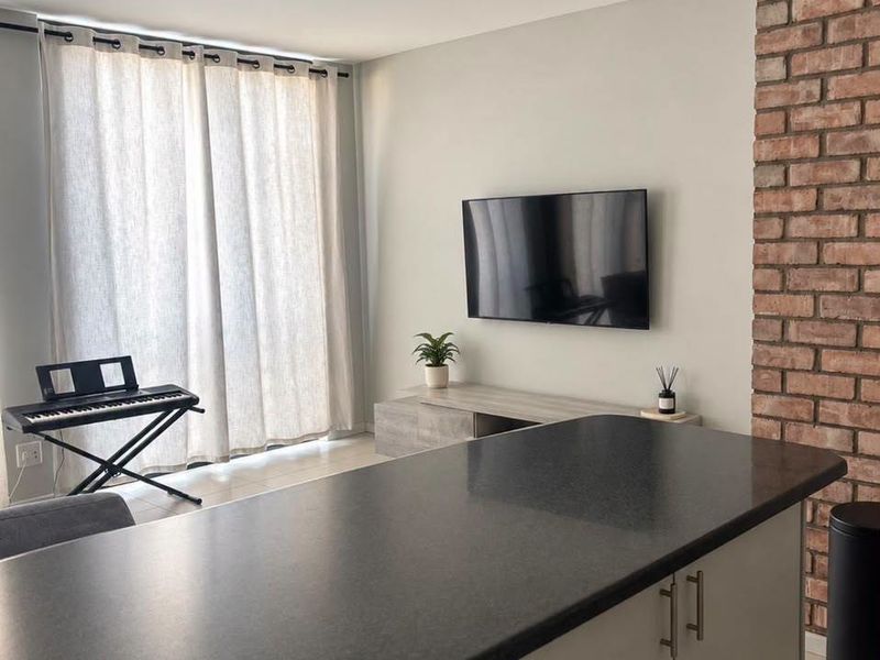 Modern open-plan living area featuring a kitchen island with dark countertops, tiled floors, and a distinctive exposed brick feature wall.