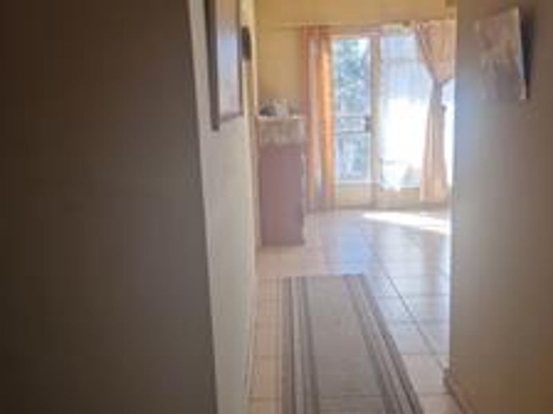A view down a tiled hallway leading towards a bright living area with a sliding glass door providing natural light.