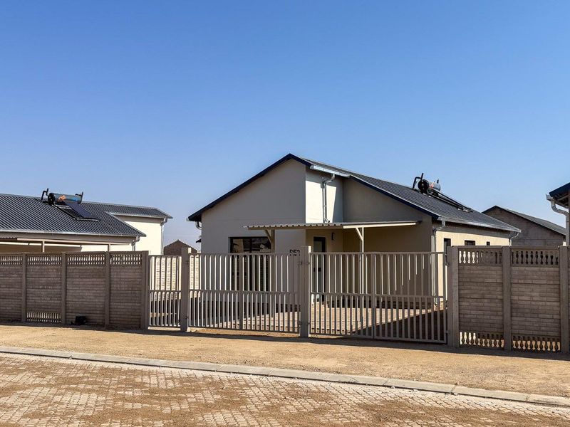 Front view of a modern single-story house featuring a metal perimeter fence, gated entrance, and a solar water heating system on the roof.