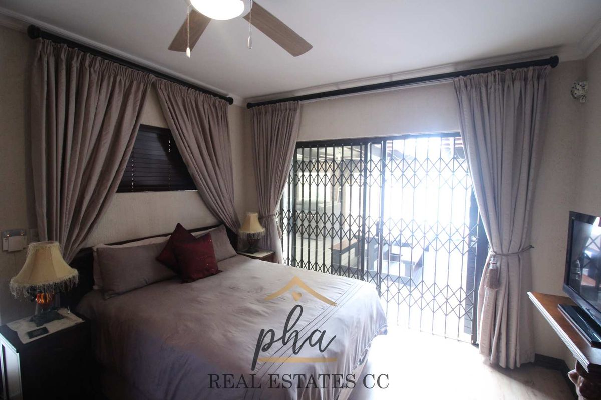 A bedroom featuring a ceiling fan and sliding glass doors with security gates, providing direct access to an outdoor area.