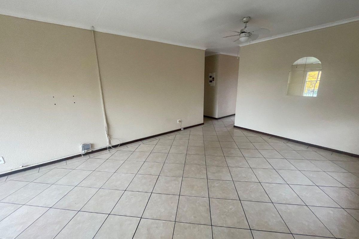 An empty, open-plan living area featuring neutral tiled flooring, a ceiling fan, and an interior archway window, requiring minor cosmetic repairs.