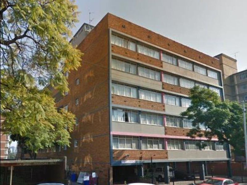 Exterior view of a multi-story brick apartment building featuring ground-level covered parking and a secure gated entrance.
