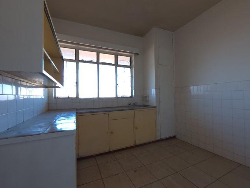 A vacant kitchen featuring original built-in cabinetry, tiled splashbacks, and tiled flooring, offering a blank canvas for a modern renovation.